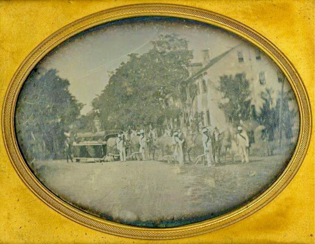 Men in uniform accompany a horse-drawn hearse.